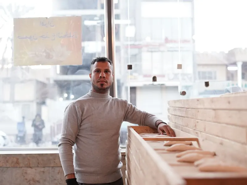 A baker beside trays of fresh bread in a bright bakery